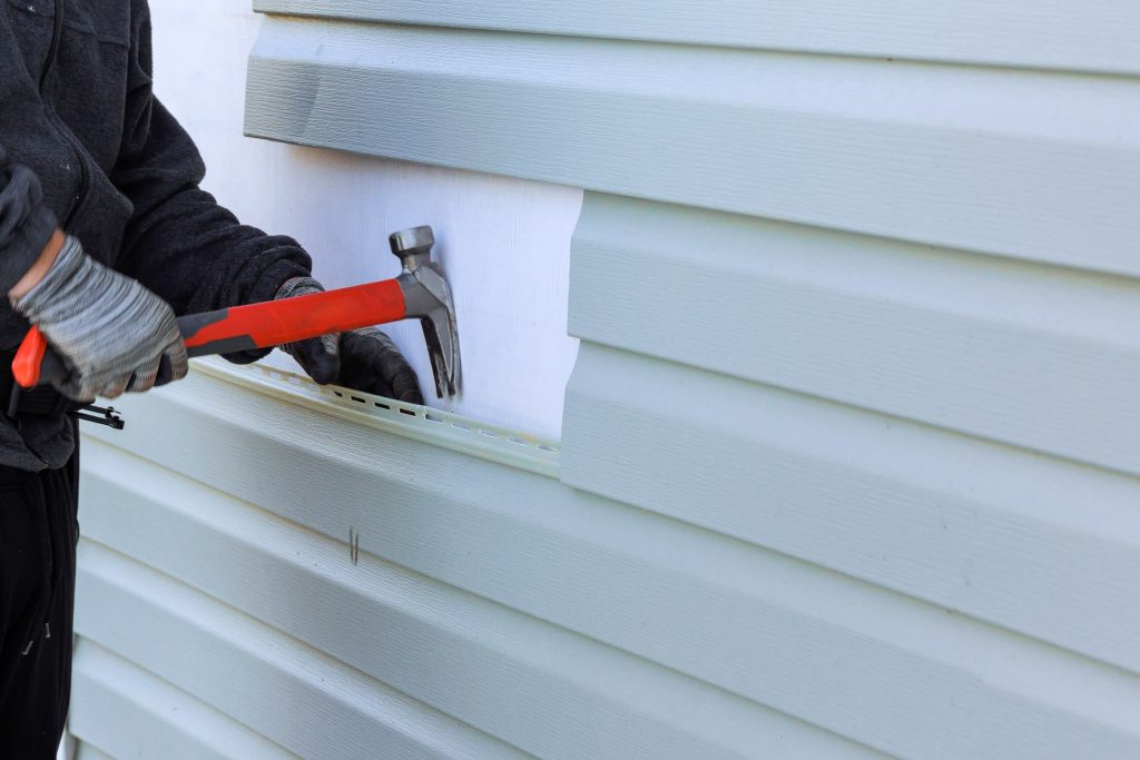 Why Siding Replacement Is the Right Time to Fix Your Home's Insulation 1 Man taking a hammer to pull off siding from the exterior of a home.